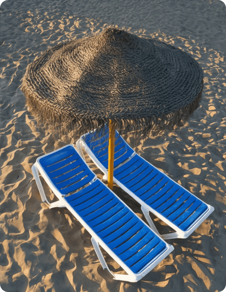 Tumbonas azules bajo sombrilla de paja en la playa de Peñíscola, servicio de playa de Hoteles Mediterráneo